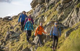 A group of hikers is walking along a rocky path. They are wearing colorful hiking attire and enjoying nature.