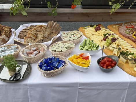 Ein reichhaltiges Buffet mit verschiedenen Brotsorten, Käse, Wurst und frischem Gemüse. Bunte Früchte und Snacks ergänzen das Angebot auf einem Tisch mit weißer Tischdecke.