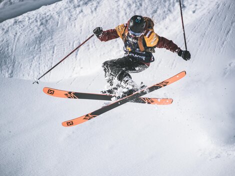 A skier jumps over a snow-covered slope. He is wearing colorful ski gear and showcasing impressive technique.