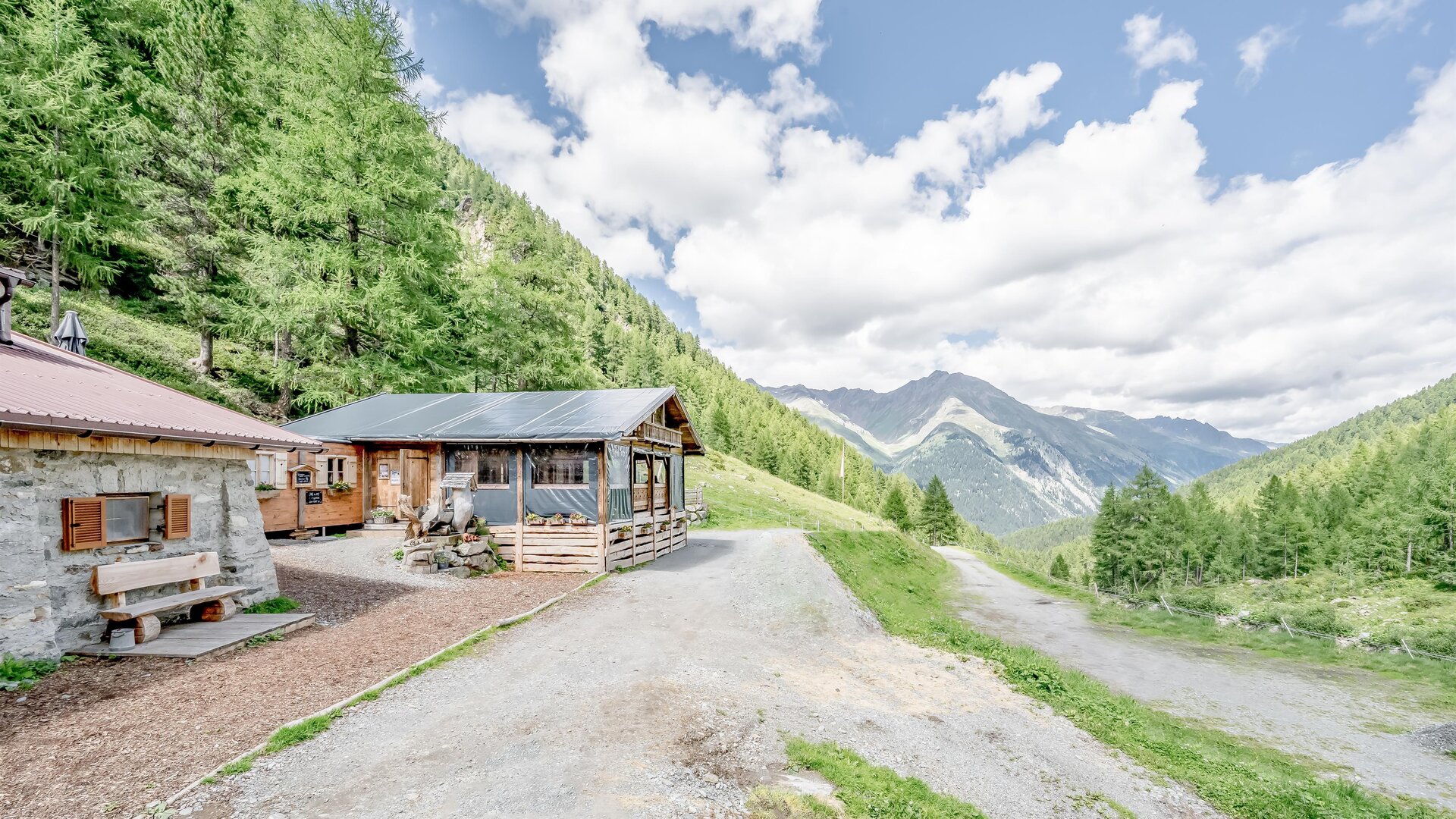 A picturesque mountain landscape with green forests and impressive peaks. In the foreground stand two cozy cabins.