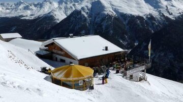 A restaurant in the mountains, surrounded by snow-covered peaks. The sunny terrace offers a beautiful view of the winter landscape.