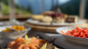 Ein ansprechend angerichteter Teller mit verschiedenen Fischsorten, garniert mit einer Zitronenscheibe. Im Hintergrund sieht man eine schöne Landschaft mit Bergen und einer klaren blauen Himmel.