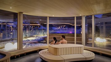 A modern spa with large windows and a relaxing atmosphere. A couple is sitting together and enjoying the view of a illuminated outdoor area.