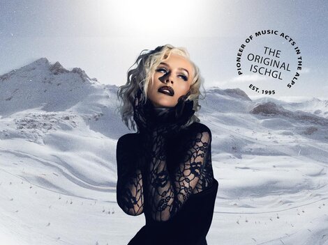 Ein glamouröses Model posiert vor einer schneebedeckten Berglandschaft. Im Hintergrund sind majestätische Berge und ein klarer Himmel zu sehen.