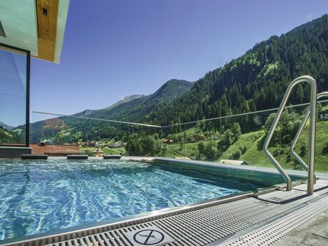 Ein moderner Infinity-Pool mit klar Wasser und Blick auf grüne Berge. Die Umgebung ist friedlich und einladend.