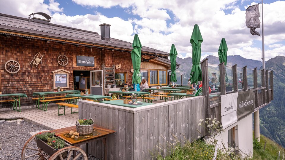 A mountain cabin with a cozy outdoor area. There are green sunshades and a beautiful view of the mountains.
