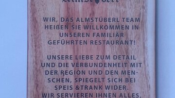 A wooden board with a welcome message for a restaurant. The text speaks of the connection to family and the importance of hospitality.