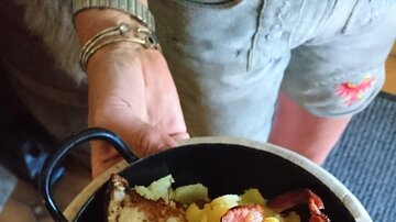 A hearty dish in a small pan, consisting of potatoes, bacon, and a fried egg. It is served by one person.