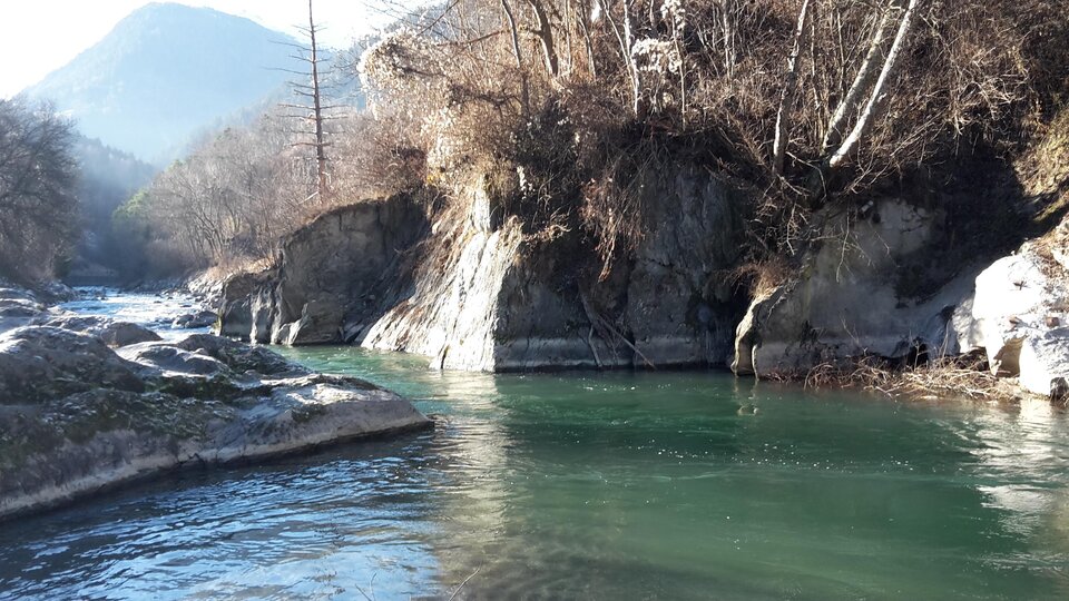 A calm river flows between rocky shores. In the background, wooded hills are visible.
