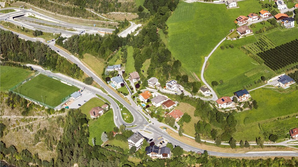 An aerial view of a rural area with residential houses, roads, and green fields. The natural environment shows a mix of residential areas and agricultural land.