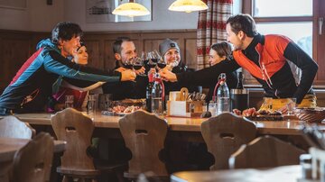A group of friends is sitting at a table in a cozy restaurant. They are toasting with glasses and celebrating together.
