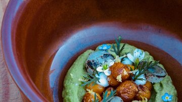 An artistically arranged dish in a brown bowl. The ingredients are garnished with fresh herbs and edible flowers.