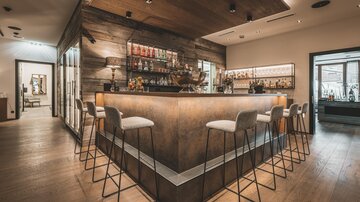 An elegant bar with a wooden design and stylish high stools. In the background, shelves with various spirits can be seen.