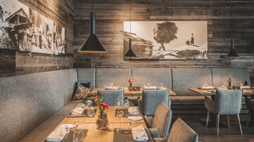 A cozy restaurant with wooden walls and stylish furniture. The tables are set with cutlery and flower decorations.