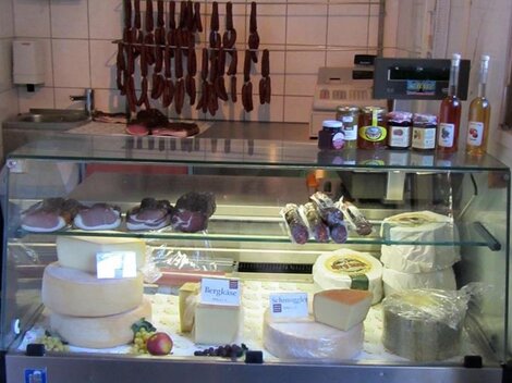 Ein Kühlschrank mit verschiedenen Käsearten, Wurstwaren und einigen Flaschen. Die Auswahl wirkt frisch und einladend.