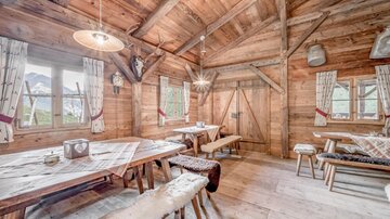 A cozy cabin with wooden interior and large windows. The room is brightly lit and contains wooden tables and benches.