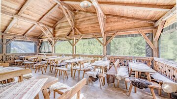 A cozy interior of a restaurant with wooden chairs and tables. Large windows offer a view of nature.