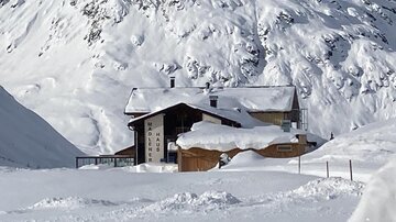 A cozy chalet, surrounded by deep snow and majestic mountains. The sky is clear and the landscape radiates tranquility.