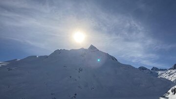 A snowy mountain landscape under blue sky. The sun shines brightly over the snow-covered peaks.