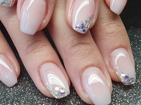 Schöne Maniküre mit zarten, rosafarbenen Nägeln und glitzernden Akzenten. Die Nägel sind sauber geformt und glänzen elegant.