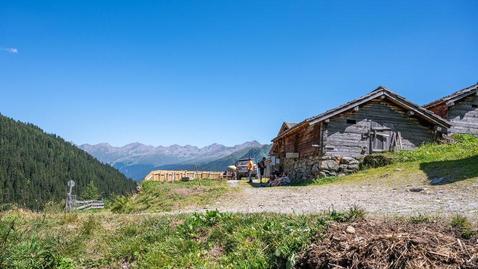 A picturesque mountain village with traditional wooden buildings and a beautiful view of the mountains. The bright blue sky and the green meadow give the scene a serene atmosphere.