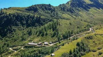 A picturesque mountain landscape with lush greenery and a small, peaceful farmhouse. In the background, a majestic peak rises under a clear blue sky.