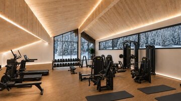 A modern gym with various training machines and mats. Large windows offer a view of a snow-covered landscape.
