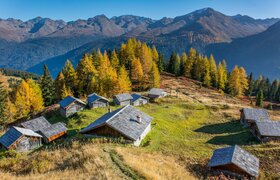 A picturesque mountain landscape with traditional huts and colorful autumn foliage. Majestic mountains rise in the background under a clear sky.
