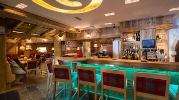 A cozy bar with rustic wooden interiors and bright lighting elements. The bar area is modernly designed and invites you to stay.