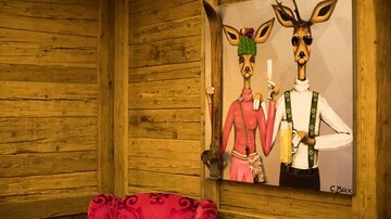 An artistic image of two stylized deer dressed in traditional attire. The wall is made of wooden panels, and in the foreground sits a red sofa.
