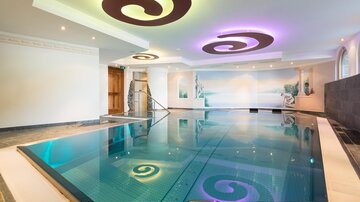An elegant indoor pool with gentle, curved patterns on the ceiling. Warm light creates a relaxing atmosphere.