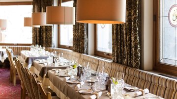 An elegant restaurant with stylishly laid tables. Soft lighting and windows create an inviting atmosphere.