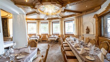 An elegant restaurant with wooden decor and large windows. The tables are festively set and invite for a cozy meal.