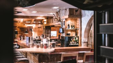 A cozy bar with wooden shelves and an inviting counter. Bottles and drinks are clearly arranged on the bar counter.